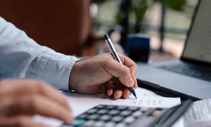 A person calculating finances with a calculator and pen on a desk indoors.