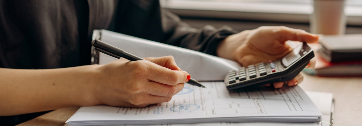 Close-up of person using a calculator with financial documents in an office.